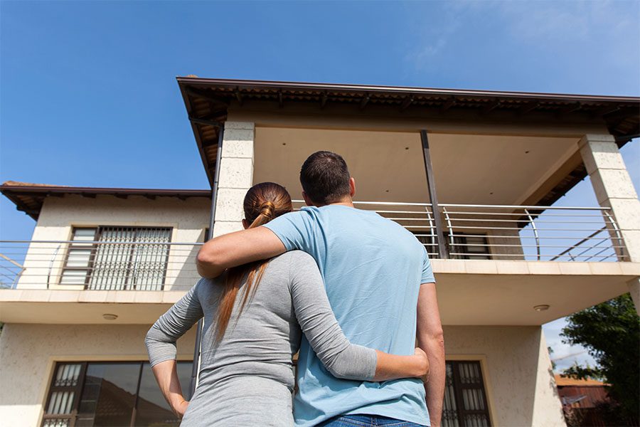 Personal Insurance - Rear View of a Happy Couple Hugging Each Other While Standing Outside and Looking at Their New Home